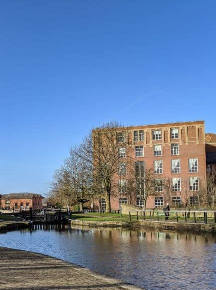 A scenic view of a historic brick building alongside a tranquil canal, surrounded by trees under a clear blue sky, highlighting the importance of locksmith services in maintaining secure properties and enhancing community safety.